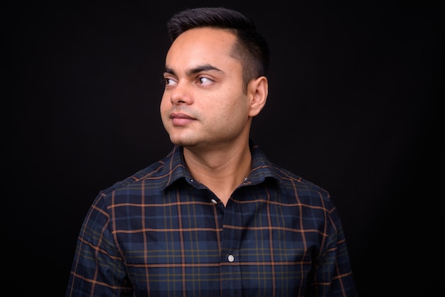  young handsome Indian hipster man against black wall