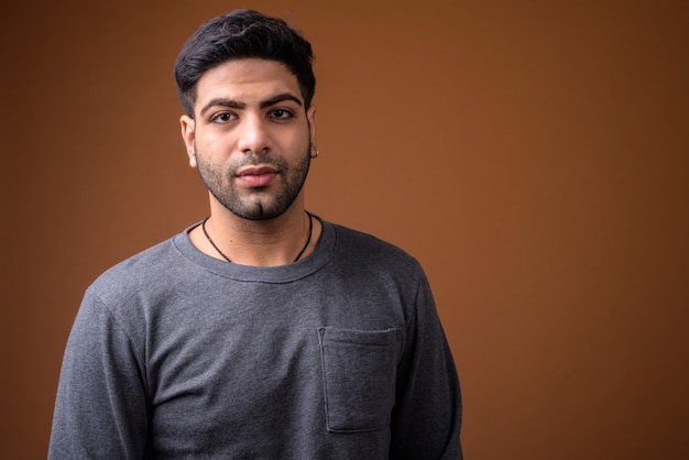 Young handsome Indian man against brown background