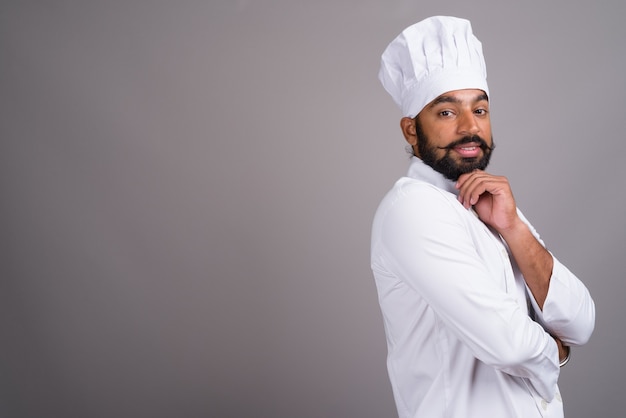 Young handsome Indian man chef on grey background