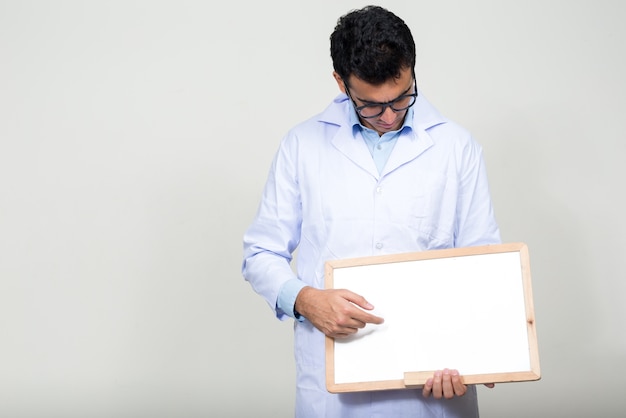 young handsome Indian man doctor against white wall