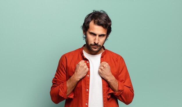 Young handsome indian man looking confident, angry, strong and aggressive, with fists ready to fight in boxing position