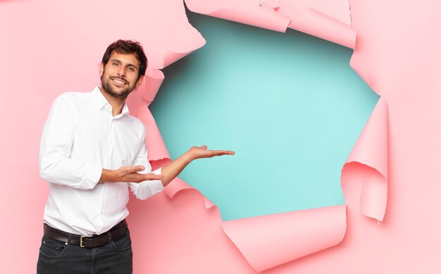 Young handsome indian man pointing or showing against broken paper hole background