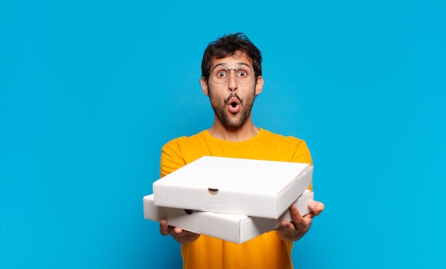 Young handsome indian man scared expression and holding take away pizzas