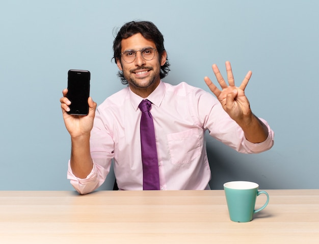 Young handsome indian man smiling and looking friendly, showing number four or fourth with hand forward, counting down. business concept