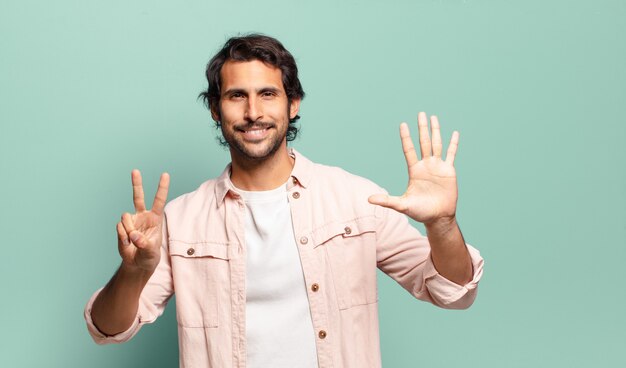 Young handsome indian man smiling and looking friendly, showing number seven or seventh with hand forward, counting down