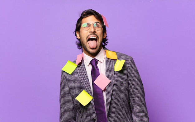 Young handsome indian man with cheerful, carefree, rebellious attitude, joking and sticking tongue out, having fun. humorous business concept