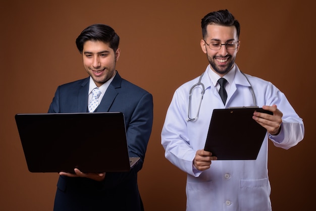 young handsome Iranian brothers together against brown wall