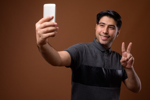 young handsome Iranian man against brown wall