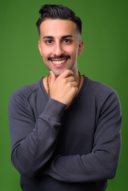 Young handsome Iranian man with mustache on green