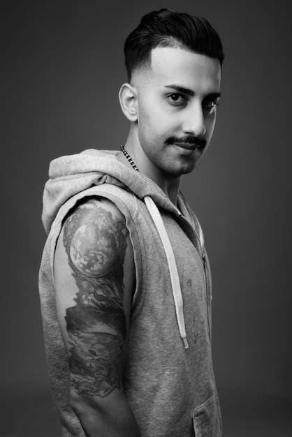  young handsome Iranian man with mustache wearing hooded shirt against gray wall in black and white