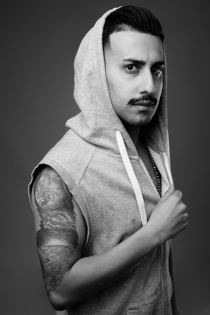  young handsome Iranian man with mustache wearing hooded shirt against gray wall in black and white