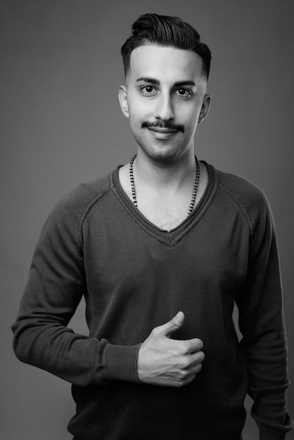  young handsome Iranian man with mustache with long sleeved shirt against gray wall in black and white