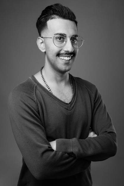  young handsome Iranian man with mustache with long sleeved shirt against gray wall in black and white