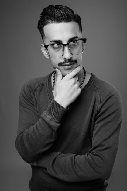  young handsome Iranian man with mustache with long sleeved shirt against gray wall in black and white