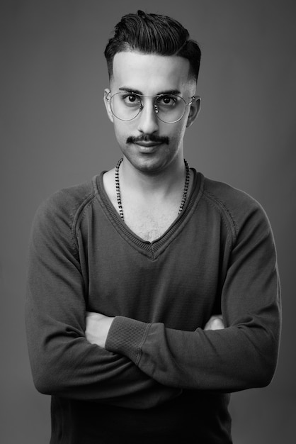  young handsome Iranian man with mustache with long sleeved shirt against gray wall in black and white