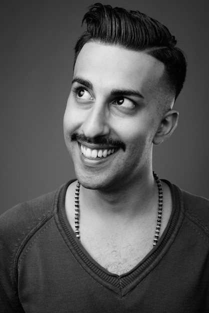  young handsome Iranian man with mustache with long sleeved shirt against gray wall in black and white