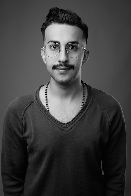  young handsome Iranian man with mustache with long sleeved shirt against gray wall in black and white