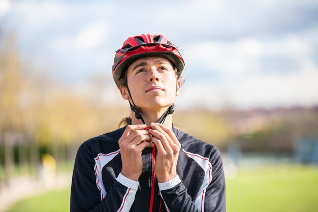 Foto giovane ciclista maschio bello in abbigliamento sportivo che si allaccia il casco protettivo nel bellissimo parco cittadino