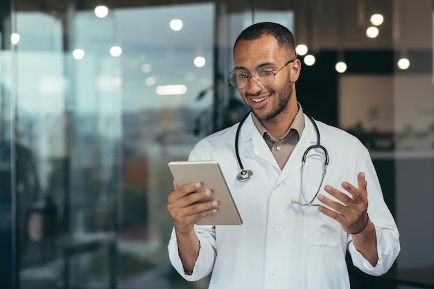 A young handsome male hispanic doctor is having an online consultation with a patient standing in