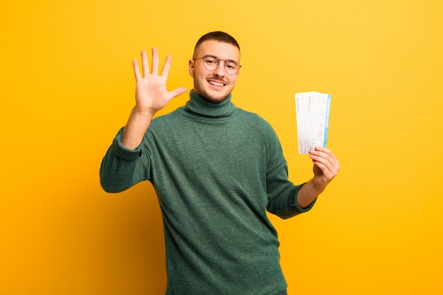 Young handsome man  against flat wall with boarding pass tickets