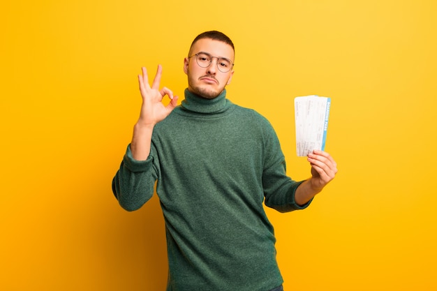 Young handsome man  against flat wall with boarding pass tickets