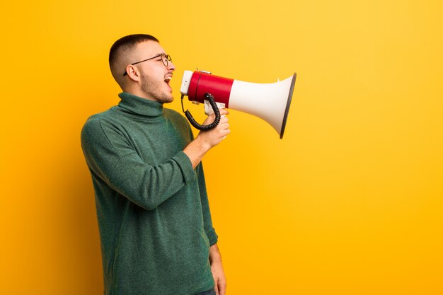 Young handsome man  against flat wall with a megaphone