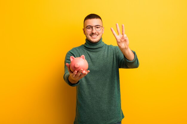 Young handsome man  against flat wall with a piggy bank