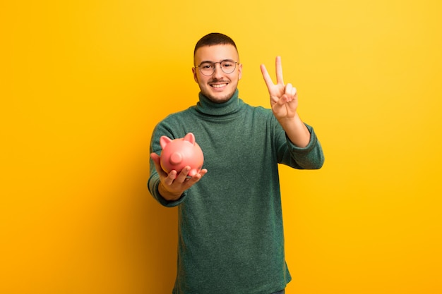 Young handsome man  against flat wall with a piggy bank