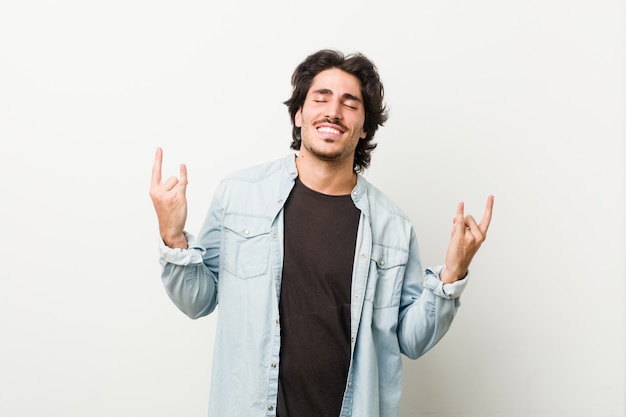 Young handsome man against a white wall showing rock gesture with fingers