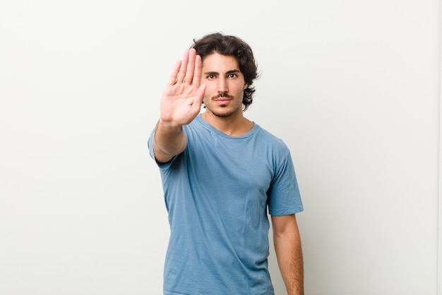 Foto giovane uomo bello contro un muro bianco in piedi con la mano tesa che mostra il segnale di stop, impedendoti.