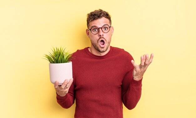 Young handsome man amazed, shocked and astonished with an unbelievable surprise. decorative plant concept