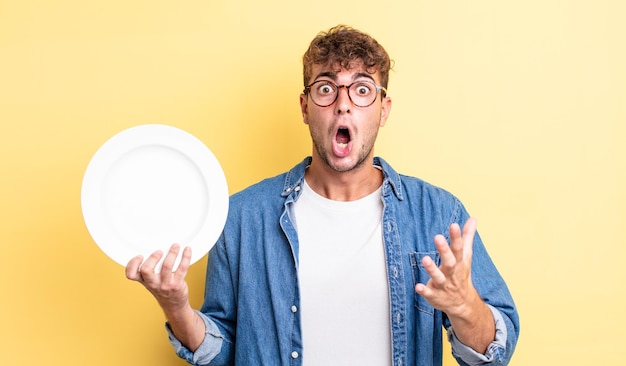 Young handsome man amazed, shocked and astonished with an unbelievable surprise. empty dish concept