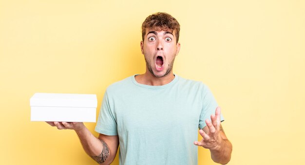 Young handsome man amazed, shocked and astonished with an unbelievable surprise. white box concept