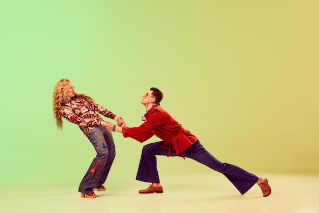 Young handsome man and beautiful woman in stylish retro clothes dancing against gradient green