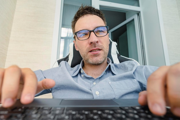 Young handsome man in a blue shirt is working at a computer on\
a light background the programmer is focused on work