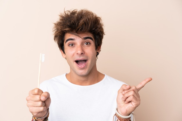 Young handsome man brushing his teeth surprised and pointing side