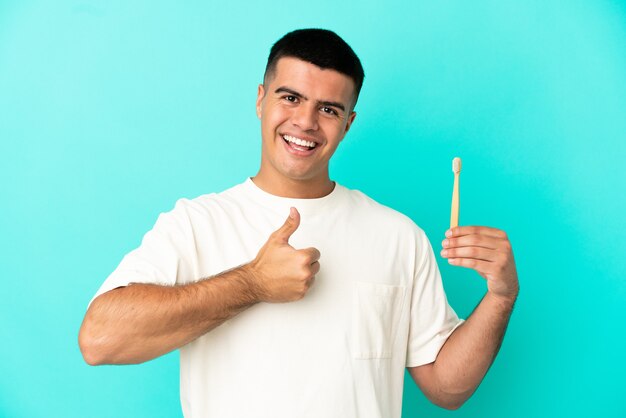 Young handsome man brushing teeth over isolated blue background giving a thumbs up gesture