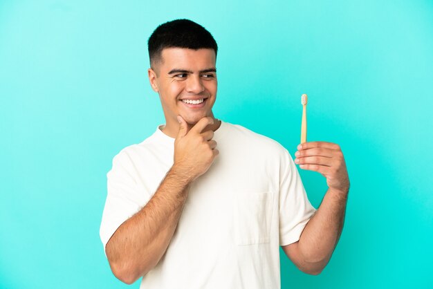 Giovane uomo bello che si lava i denti su sfondo blu isolato guardando di lato e sorridente