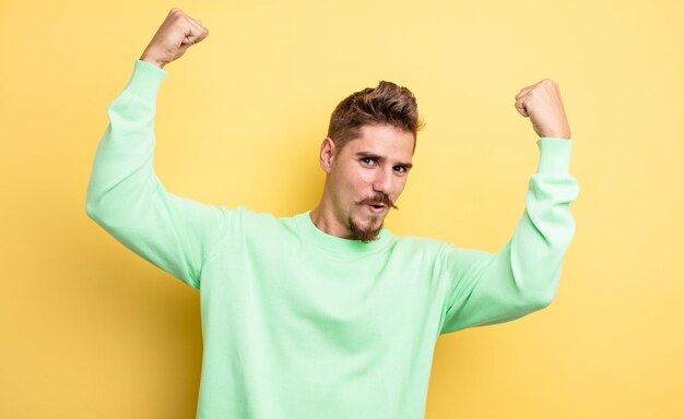 Young handsome man celebrating an unbelievable success like a winner, looking excited and happy saying take that!. strange moustache concept