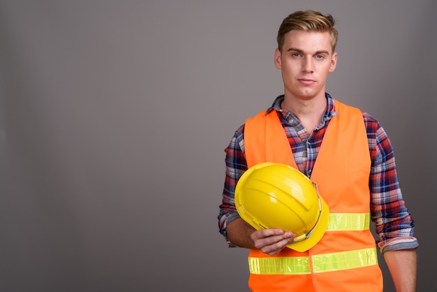 Young handsome man construction worker with blond hair on grey wall