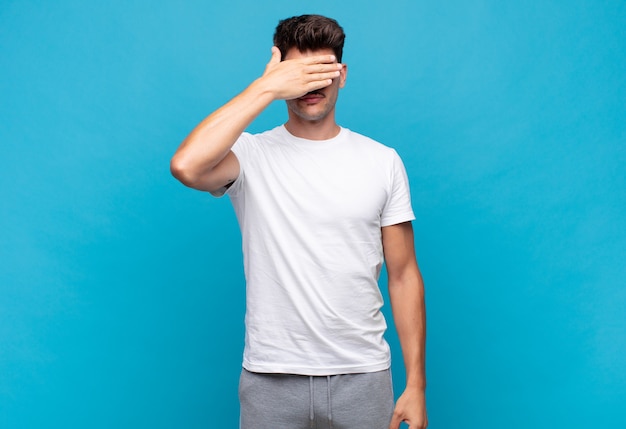 Young handsome man covering eyes with one hand feeling scared or anxious, wondering or blindly waiting for a surprise