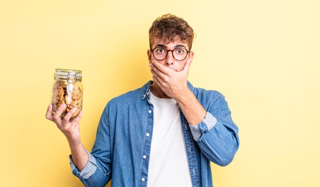 Young handsome man covering mouth with hands with a shocked. cookies bottle concept