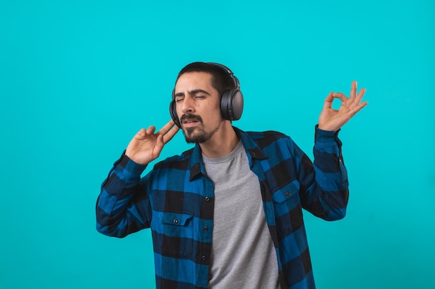 Young handsome man dancing and singing songs listening to music in headphones on a blue background