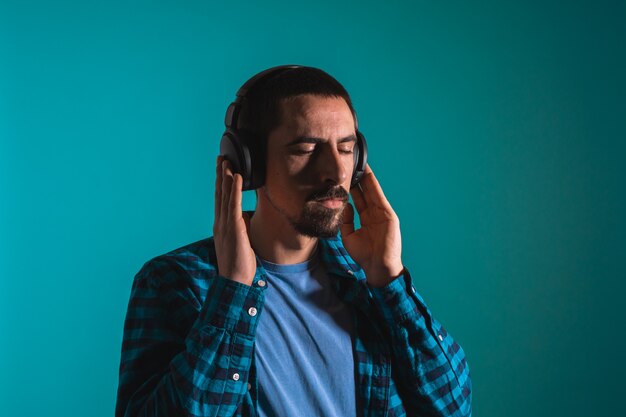 Young handsome man dancing and singing songs listening to music in headphones on a blue background