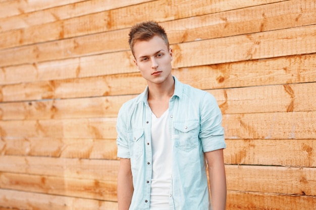 Young handsome man in a denim dress near the wooden wall