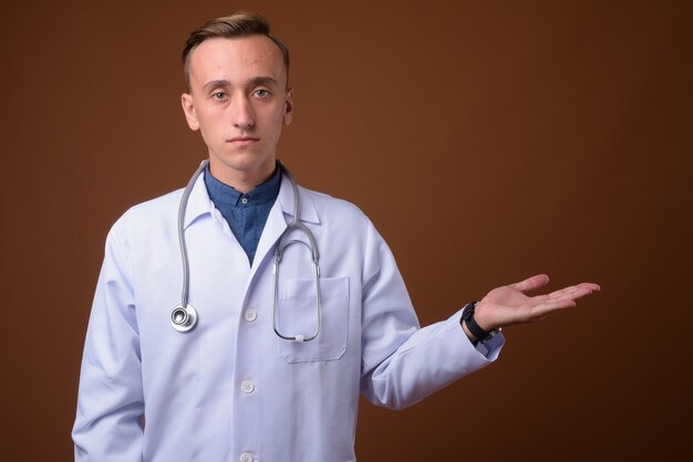 Photo young handsome man doctor against brown