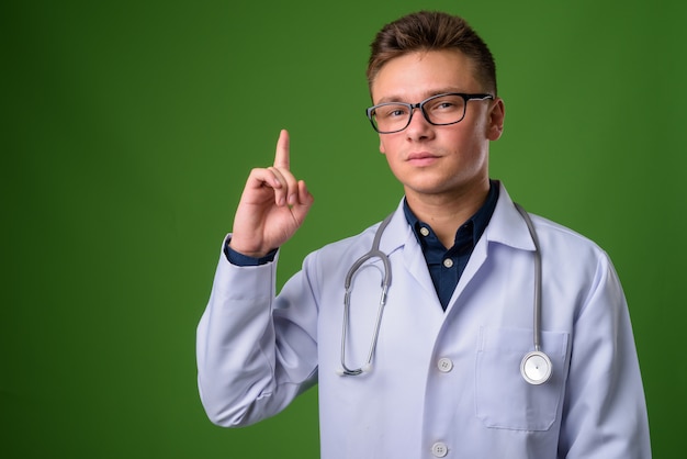 Young handsome man doctor against green background