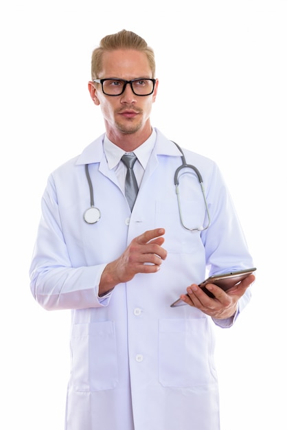 Young handsome man doctor holding digital tablet while thinking