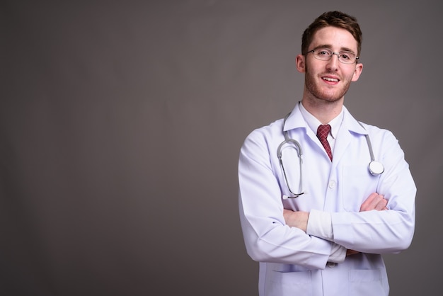 Young handsome man doctor wearing eyeglasses against gray