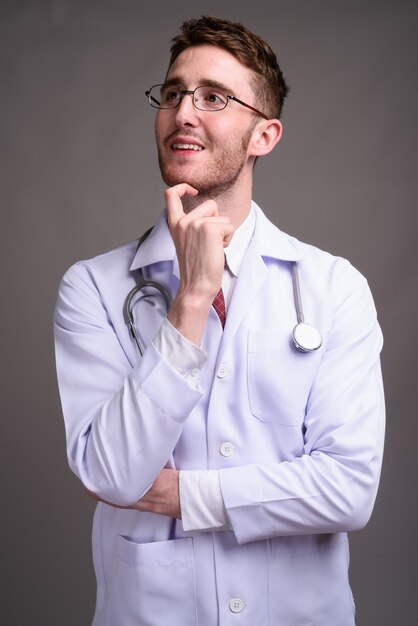 Young handsome man doctor wearing eyeglasses against gray